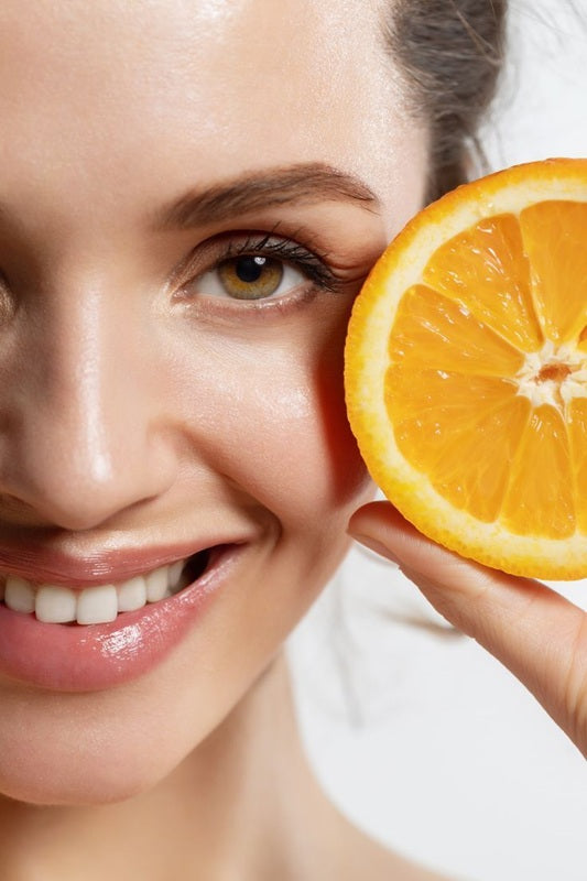 Woman holding a sliced orange near her face on a white background